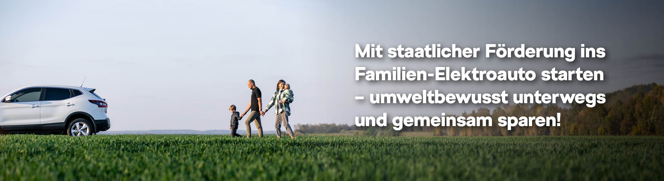 Ein weißes Auto steht auf einer Wiese. Daneben läuft eine Familie mit zwei kleinen torsichtungen durch das grüne Gras, im Hintergrund ist ein weiter, offener Himmel zu sehen. 